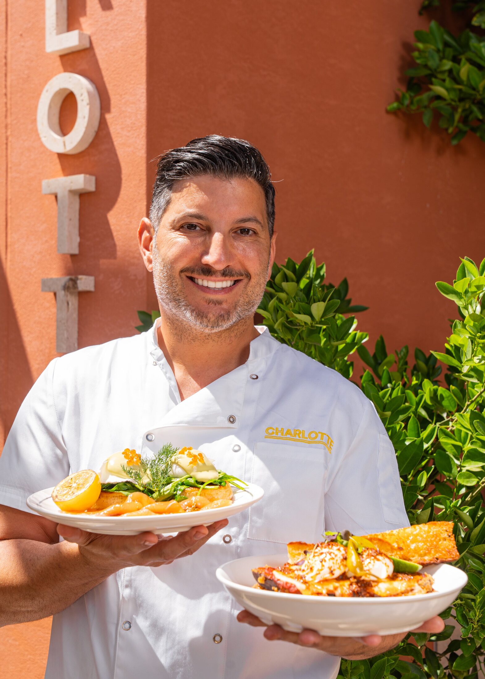 Charlotte chef holding dishes in front of the Charlotte terracotta wall