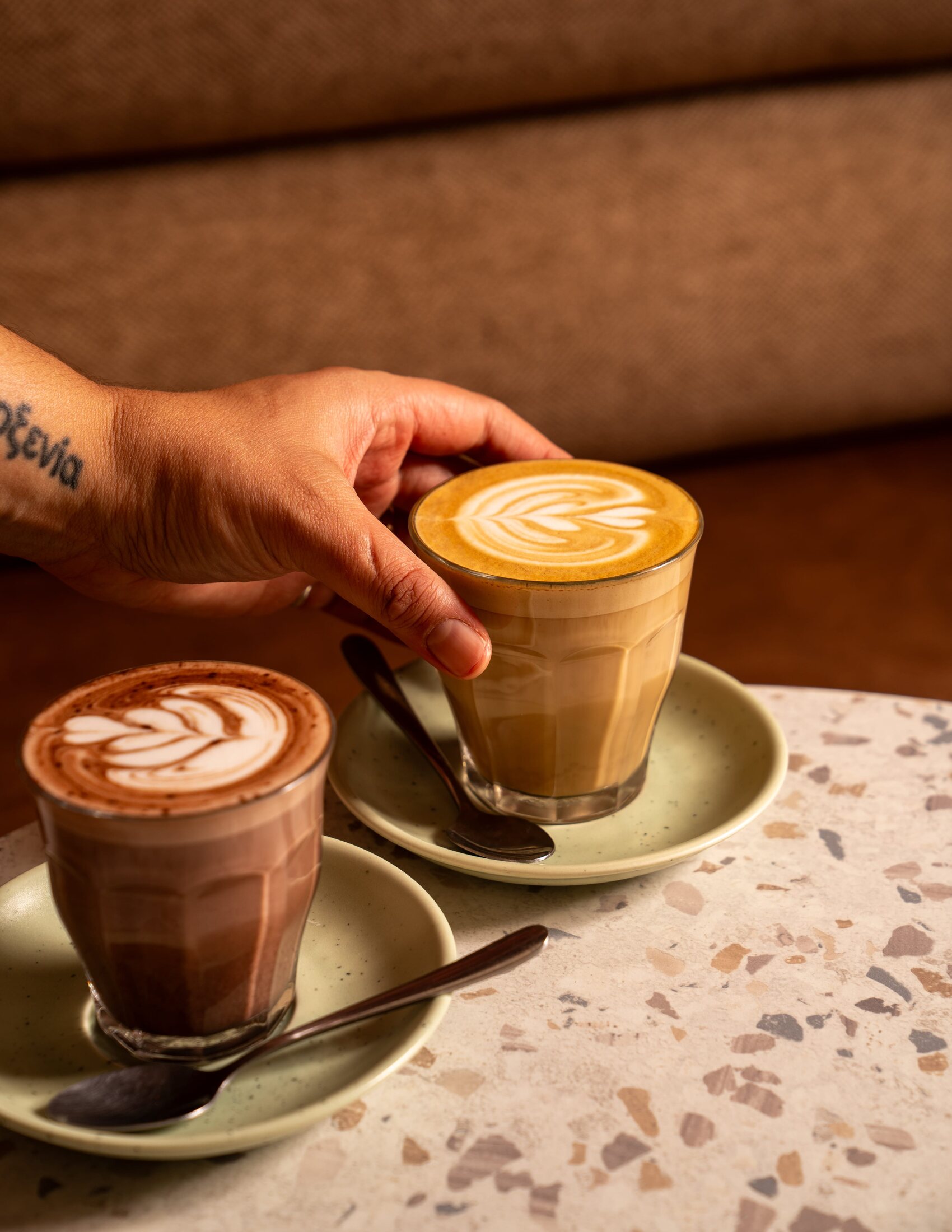 Two Charlotte coffees with latte art on sage green saucers